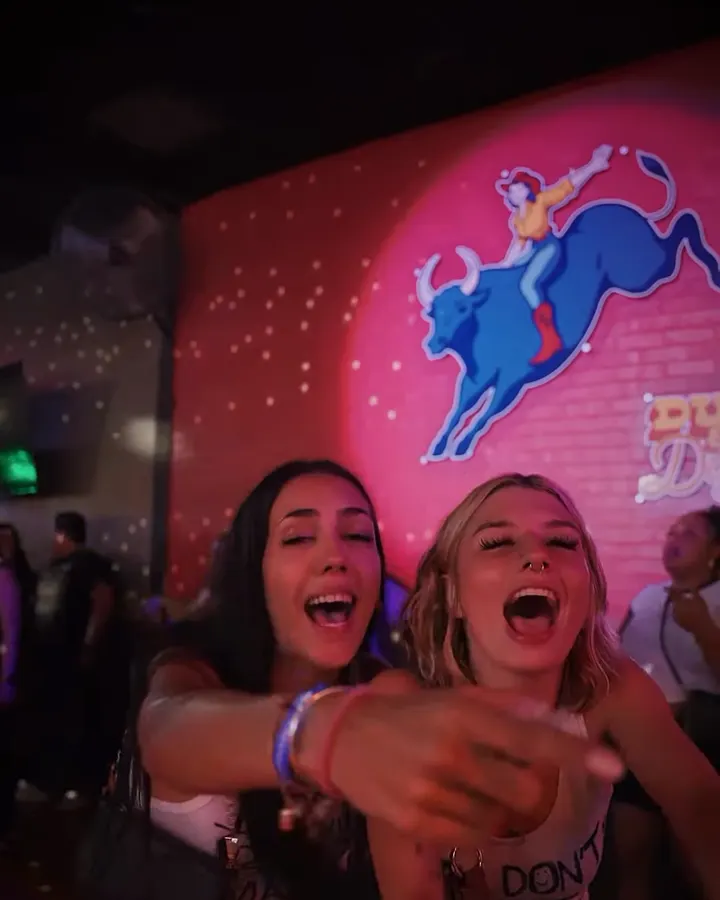 Two friends laugh in front of the pink bull rider mural