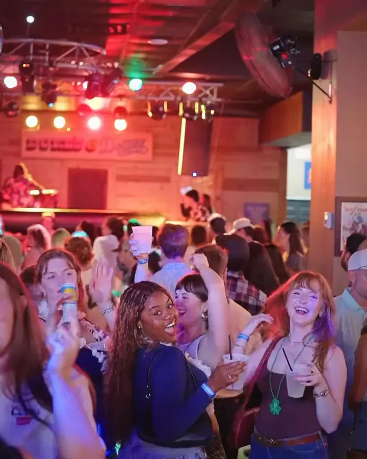 Friends laugh and raise their cups in a crowd below the stage lights