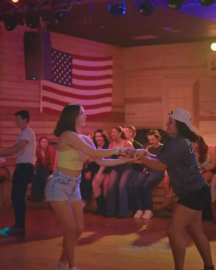 Two dancers swing each other around the floor in front of an American flag and pine walls